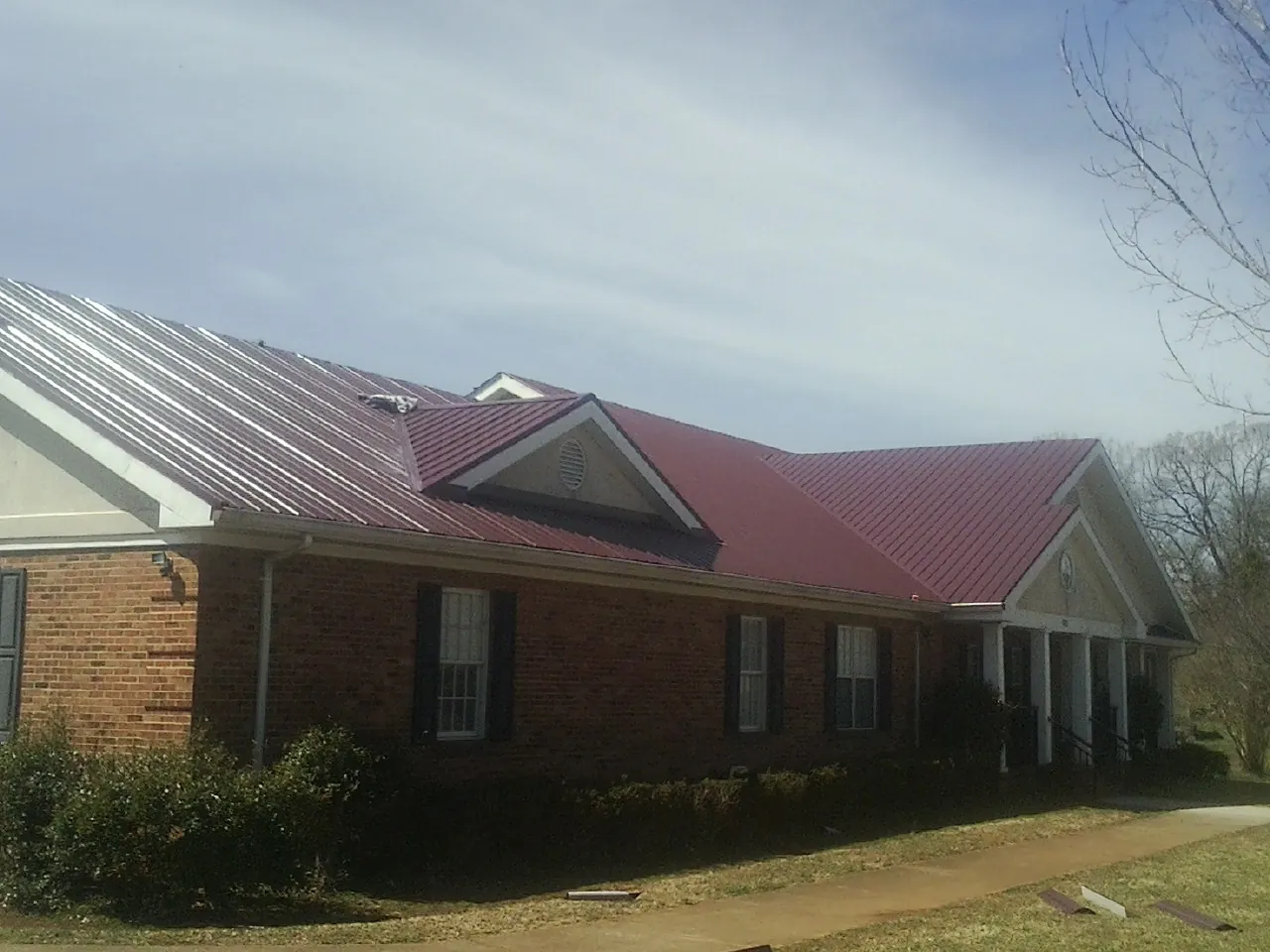 Red metal roof with gabled entries on a long brick building, from a Hail Damage Roof Repair job in San Francisco