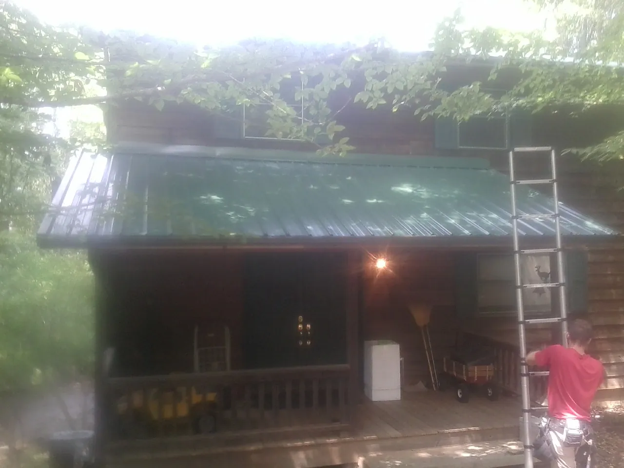Worker on a ladder at the green porch roof of a wooded cabin in San Francisco
